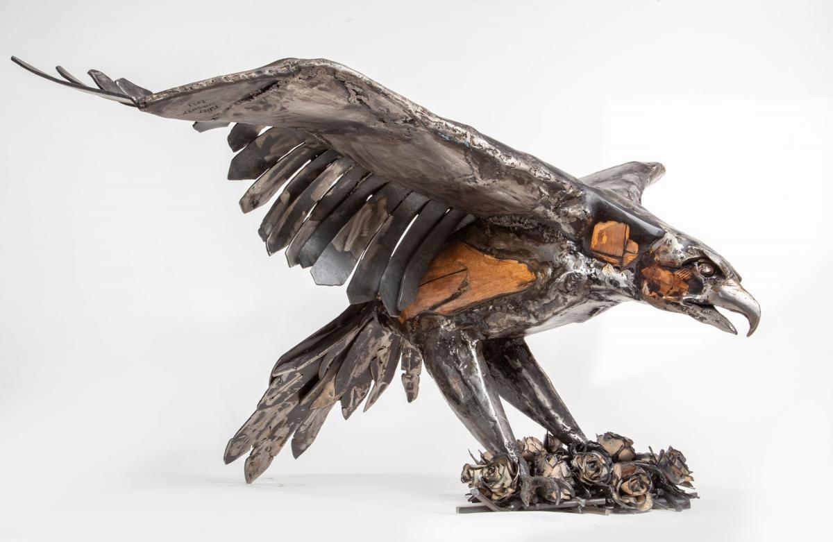 Raptor on Roses Hand built steel and wood sculpture of an eagle raptor landing on a bed of roses. The raptor’s wingspan is as wide as a 5’ tall human. The raptor’s legs are stretched down towards the ground as it lands in a bed of steel roses. I made the roses out of reclaimed steel from the old electrical panel on my house and my wife’s antique steel baking sheets (she told me she was ready to donate her collection to a sculpture). The tail feathers are down, the beak is slightly open.
