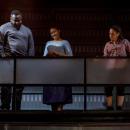 ive people standing looking down in the order of: white male in red top, a black male in gray top, a female in light blue dress, a female in light maroon top with dark pants and a white male in dark color top.