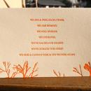 Photo of a postcard with orange letters and floral patterns on the bottom.