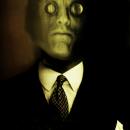 A scanograph, photomontage color self- portrait depicting me with a lizard’s face with magnifying lenses over my eyes. I am wearing a business suit and tie. This image is from my “Transmog Project” body of work.