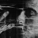 A black & white self-portrait scanograph from my “Blind Vision” series. The image depicting a profile of my face and my hand with fingers spread. My eyes are closed and I am wiping away white foam which is streaked across my face and the image frame. The white foam represents the obstructions I experience in my vision.
