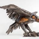 Hand built steel and wood sculpture of an eagle raptor landing on a bed of roses. The raptor’s wingspan is as wide as a 5’ tall human. The raptor’s legs are stretched down towards the ground as it lands in a bed of steel roses. I made the roses out of reclaimed steel from the old electrical panel on my house and my wife’s antique steel baking sheets (she told me she was ready to donate her collection to a sculpture). The tail feathers are down, the beak is slightly open. 