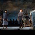A black female cop, a white male with dark pants and plaid shirt with suspenders, and a black male in overalls are looking up.